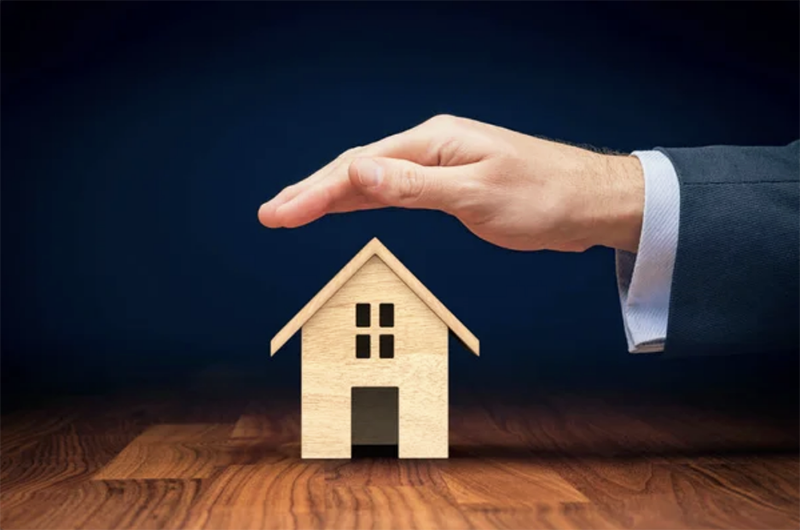 A hand covering a miniature house representing home insurance - 1 (800) 880-7954